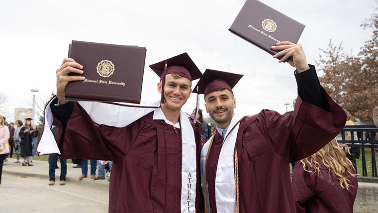 Two BearGrads holding up their diploma covers after commencements