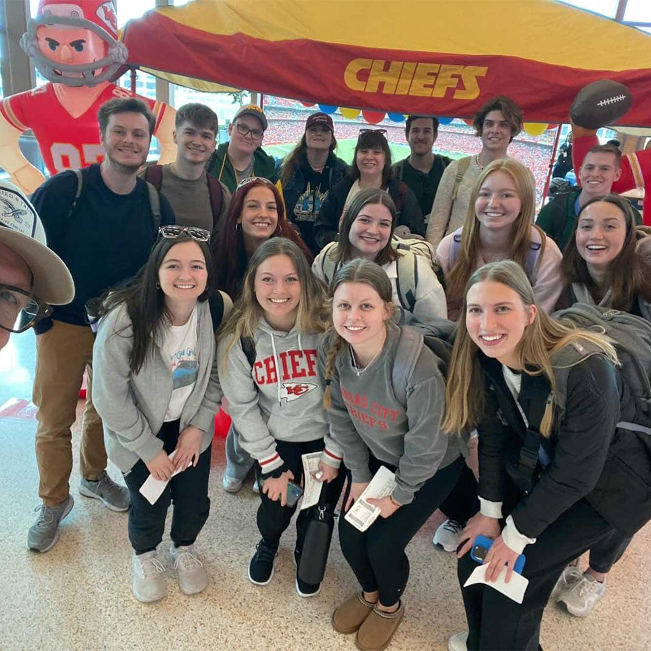 Sixteen MSU students assemble for a group picture under a Chiefs-themed canopy at the big game.