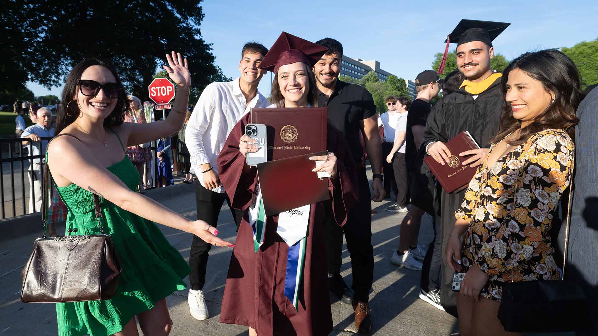 A #BearGrad holding up her diploma cover poses with friends and family following commencement ceremonies.