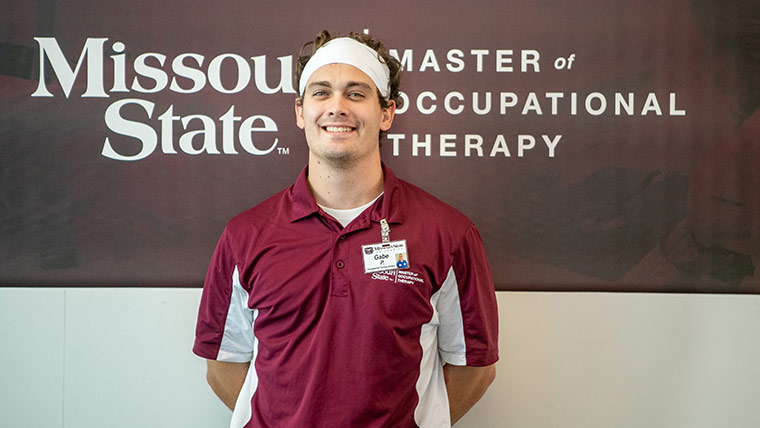 Occupational therapy student posing in front of Missouri State Master of Occupational Therapy sign inside of O’Reilly Clinical Health Sciences Center.