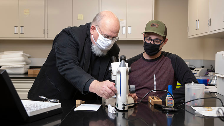 Student and professor using microscope in lab.