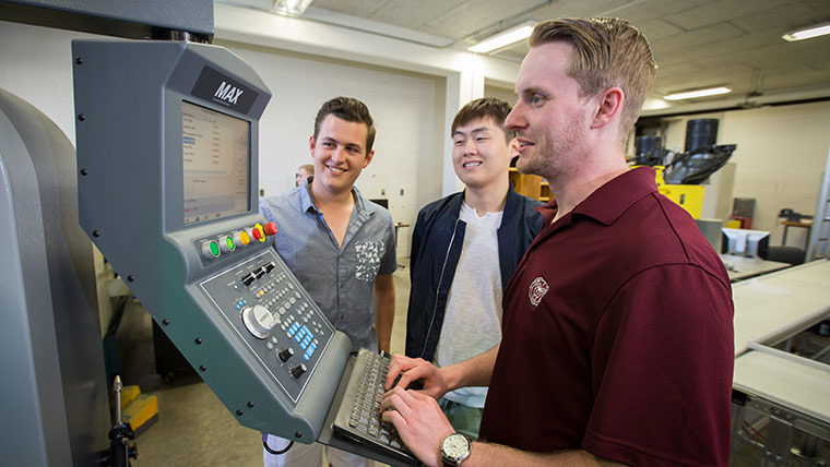 One student using the controls for a mechanical system while two other students watch.