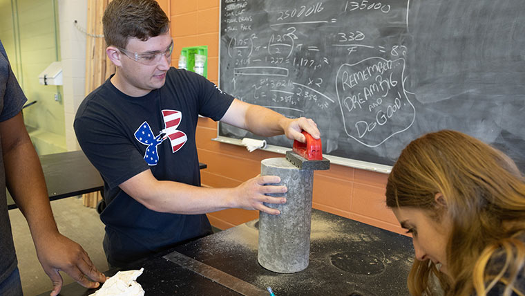 Dr. Matt Pierson lifts a concrete cylinder block as students watch.