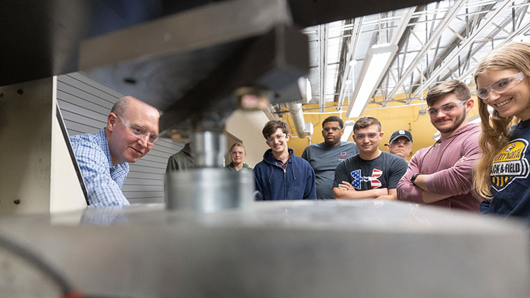 Dr. Matt Pierson and students watching a machine test concrete during a lab class.