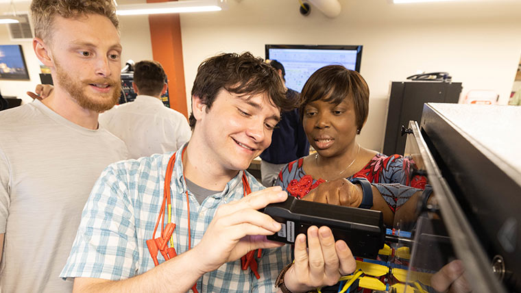 Dr. Theresa Odun-Ayo and two electrical engineering students looking at the results displayed on a device during a lab.