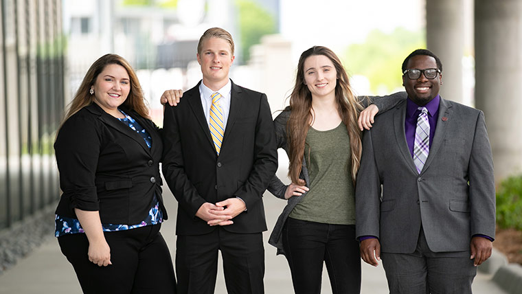 Four MSU business students dressed in professional attire outside of Glass Hall.