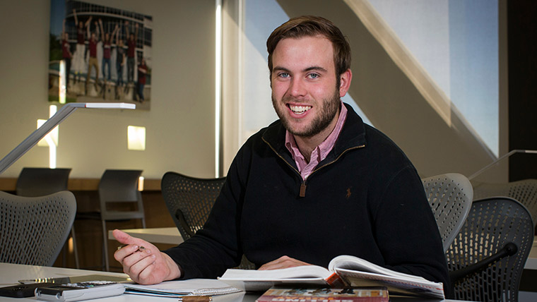 A financial planning student looks up to smile while studying from a textbook.