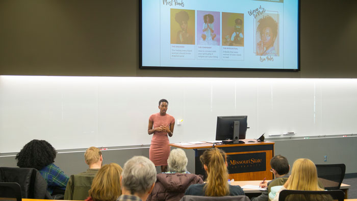 Wide-angle view of Maya Sudduth presenting senior project for her individualized major