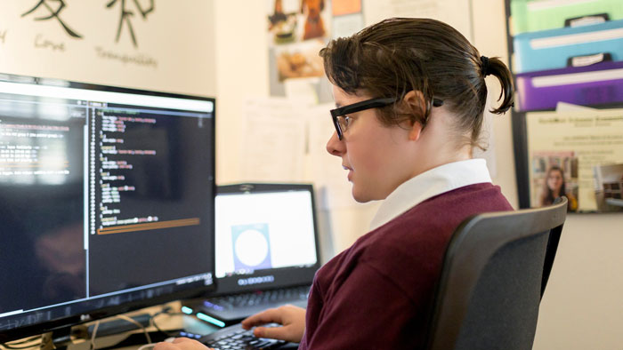 Madison Estabrook sitting at computer desk with coding information displayed on the monitor