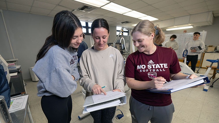 Three Missouri State students reviewing papers on a binder.