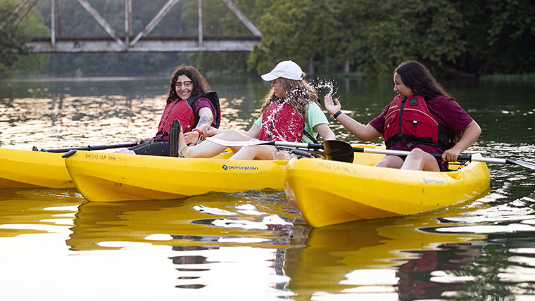 Two students in separate kayaks giving each other a high five