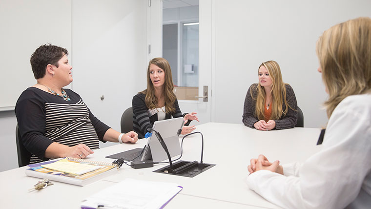 Nursing students and an instructor engage in a class discussion at a table.