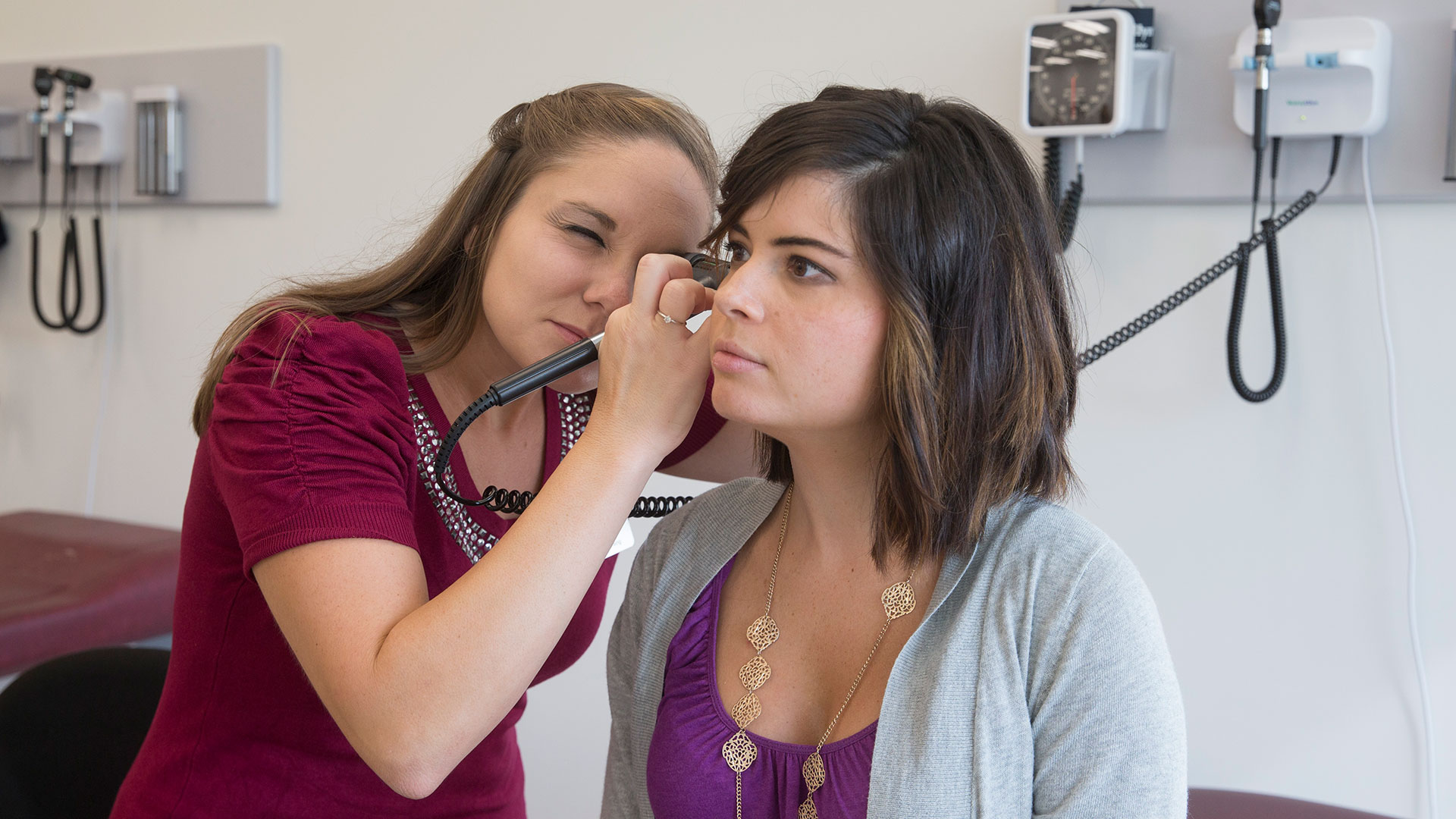 A nursing student checks inside her patient's ear with an otoscope.