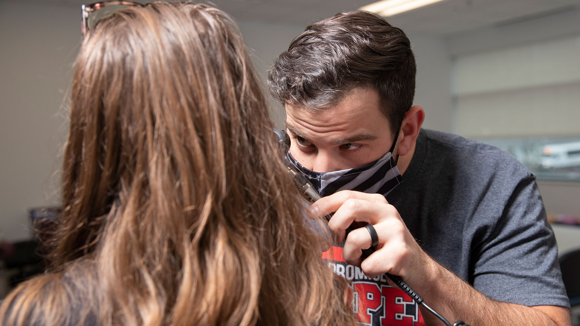 A graduate nursing student uses an otoscope to look into his patient's ear.
