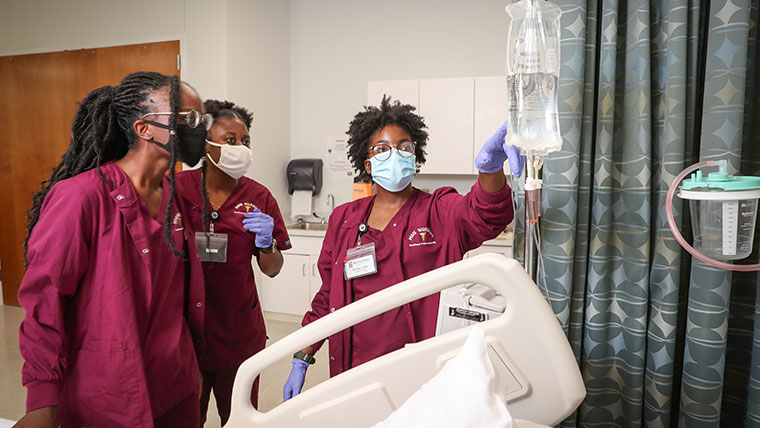 Three nursing students monitor the level of the fluid in an IV bag.