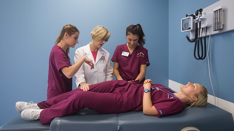 A teacher helping three nursing students in a lab.