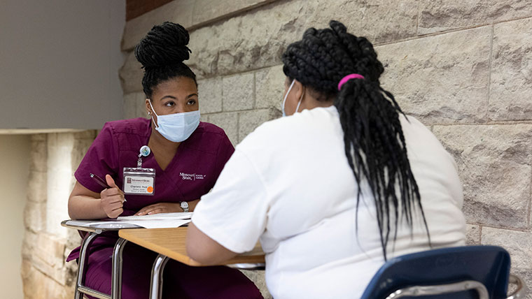 A Missouri State nursing student takes notes at a table across from a Central High School student as part of a mentorship program.