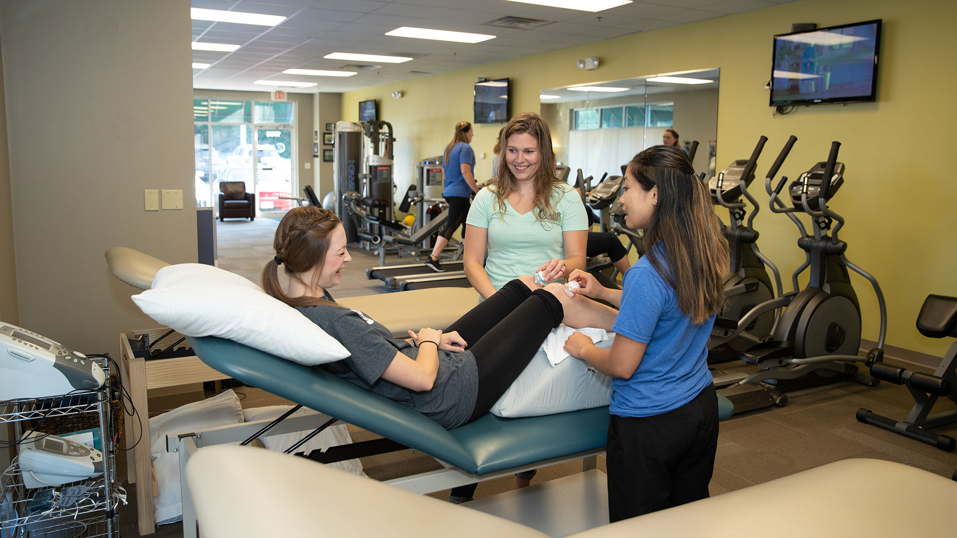 Two physical therapy students treat a person's injured knees with ice.