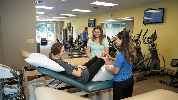 Two physical therapy students treat a person's injured knees with ice.
