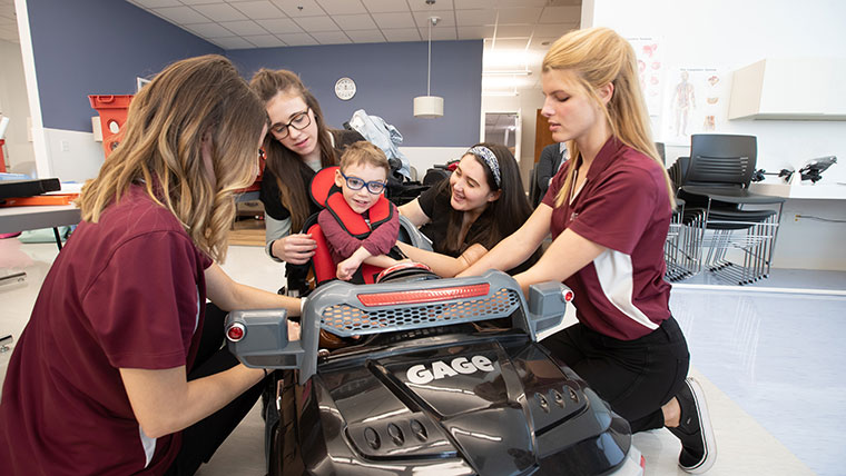 Occupational therapy students secure a child into a car seat.