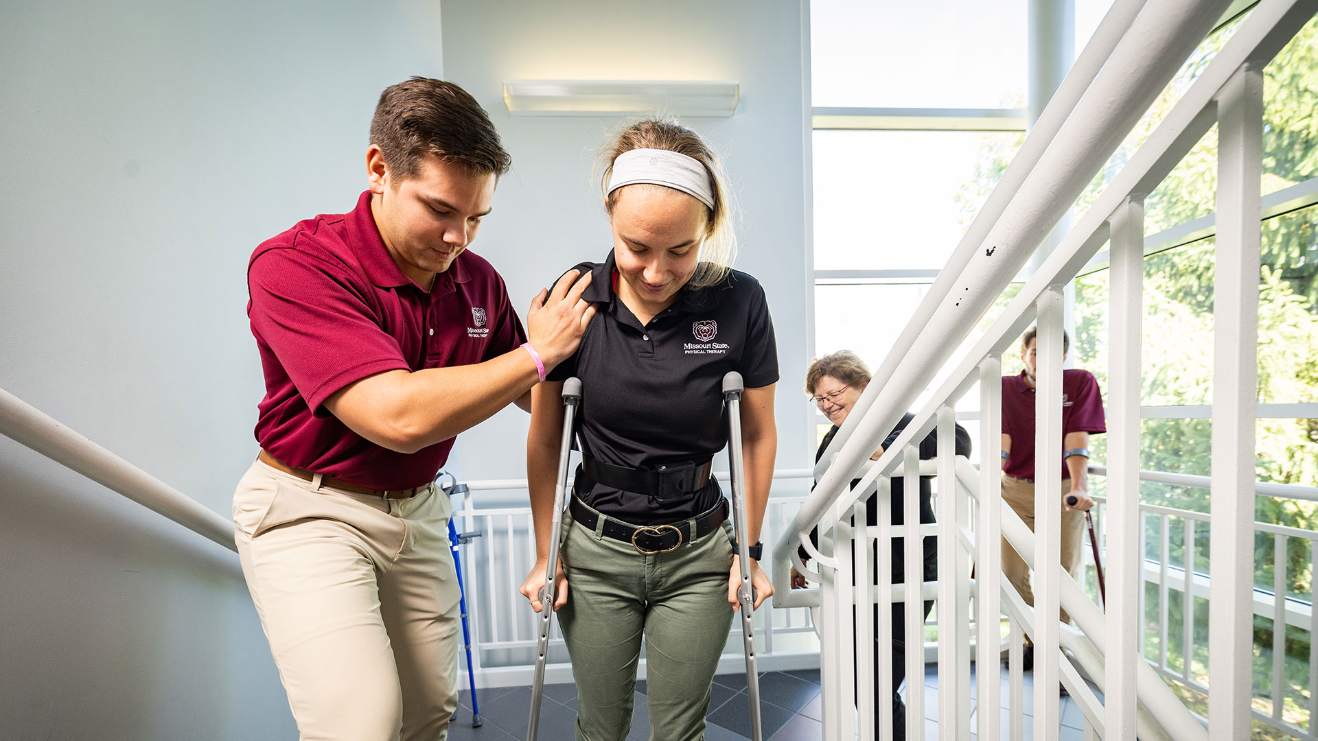 A physical therapy student practices helping another student use crutches.
