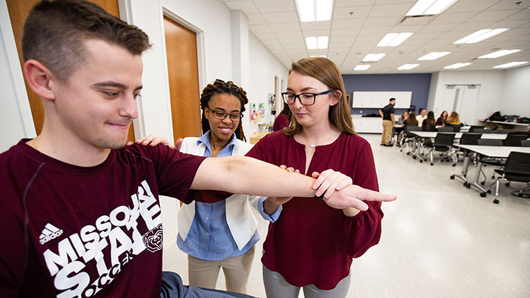 Two athletic training students stretch another student's arm.