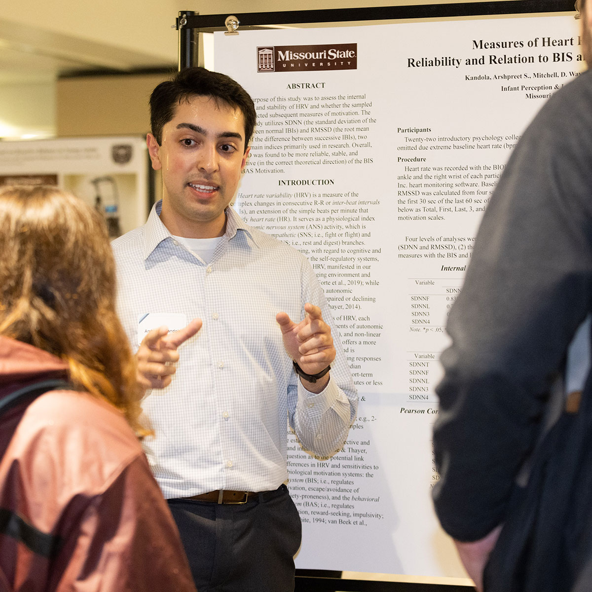 A graduate student shares his poster presentation with two listeners at a research symposium