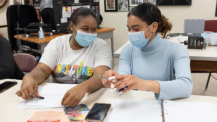 Psychology student mentoring high school student in classroom.