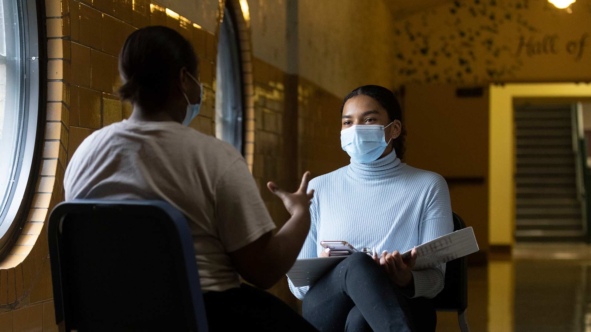 Psychology student talking to high school student in hallway.