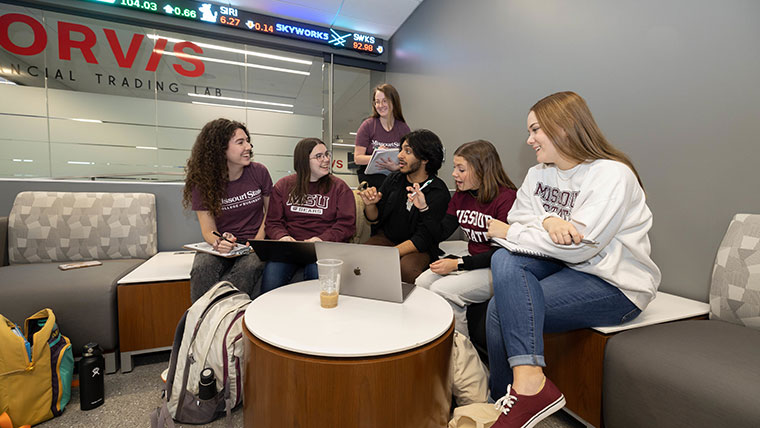 A group of MSU accounting students enjoy a stimulating conversation while studying with their notebooks and laptops in a financial trading lab.