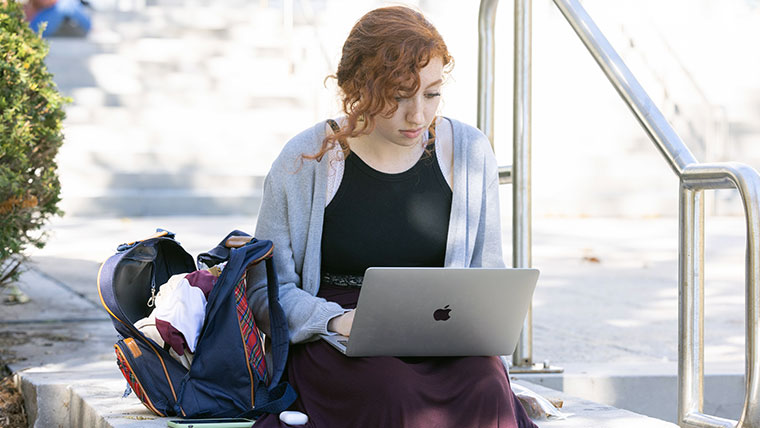 Missouri State student sitting outside looking at their laptop.