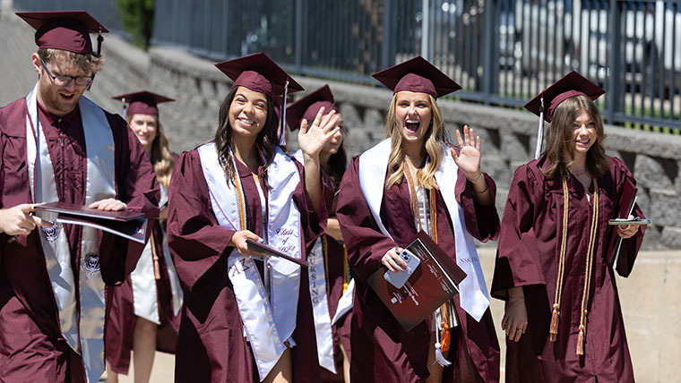 Missouri State students at commencement in cap and gown smiling and waving.