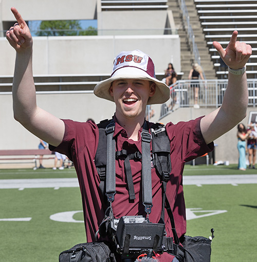 Smiling photographer in BearWear with fingers pointing to the sky.