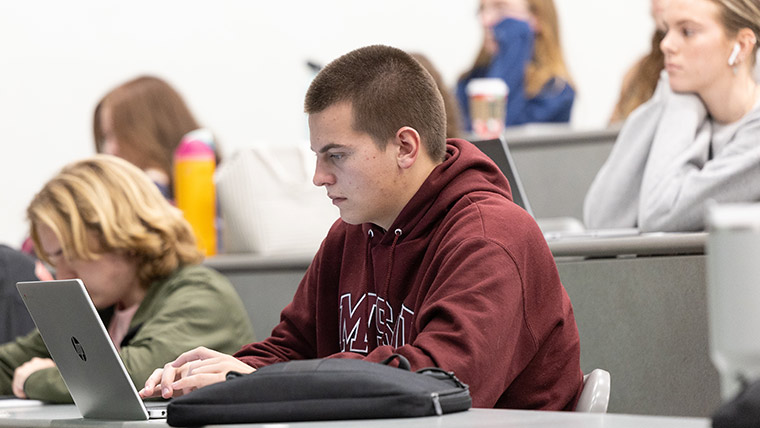 Student in a maroon Missouri State hoodie using a laptop  during class.