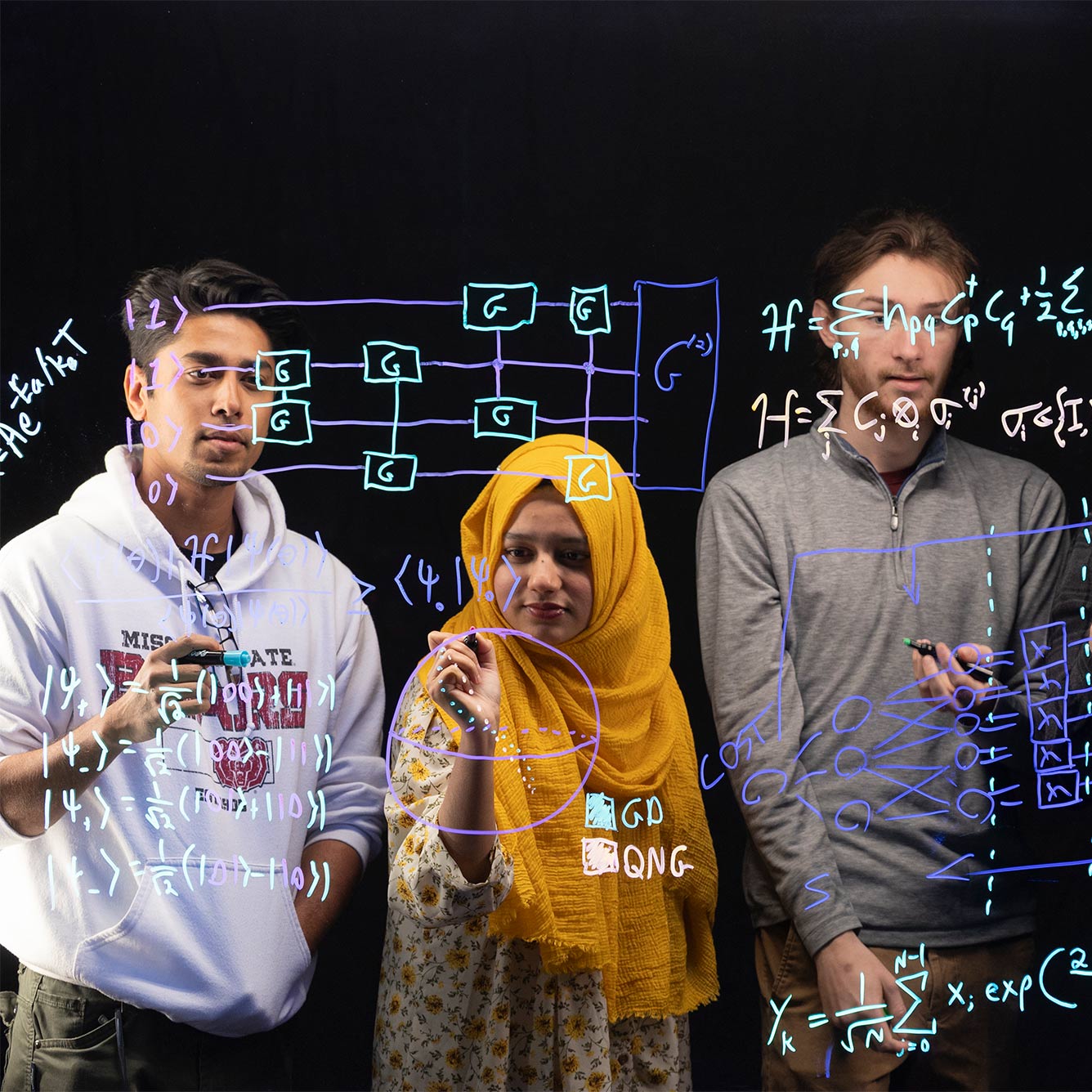 Three students study equations on a transparent markerboard for a quantum circuit design project.