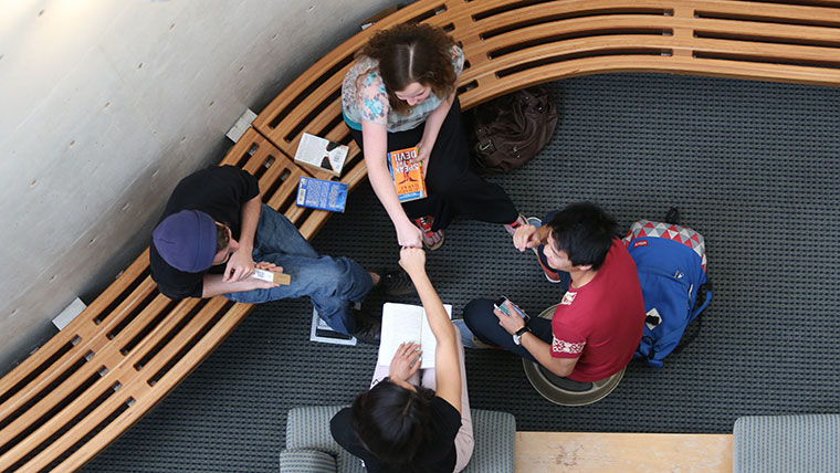 Four students study in a circle. Two of the students bump fists.