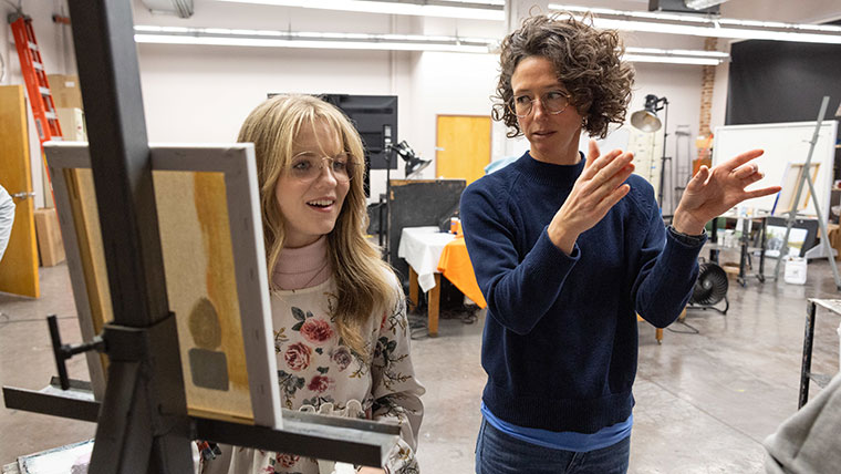 Professor Sarah Williams provides instruction to an art student during a painting class.