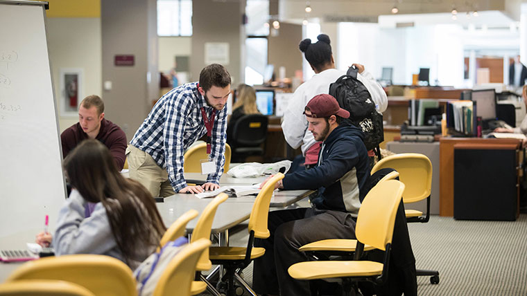 A library student worker assists another student with his classwork